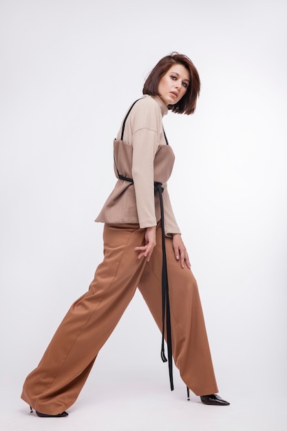 Mujer en corsé de traje marrón y beige posando sobre fondo blanco Corte de pelo Bob Foto de estudio