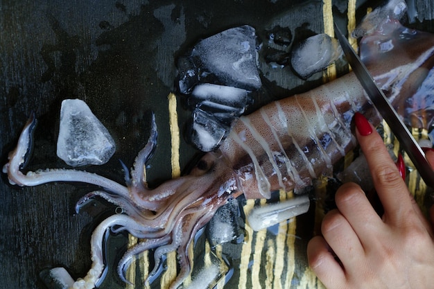 Una mujer corta calamar fresco en anillos con hielo triturado sobre un fondo oscuro.