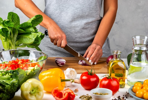 Mujer corta cebollas y hace ensalada en la cocina