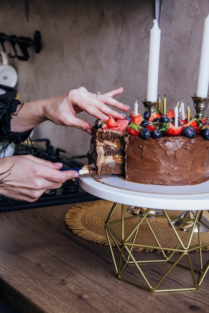 Una mujer corta un pastel de chocolate con fresas y arándanos encima.