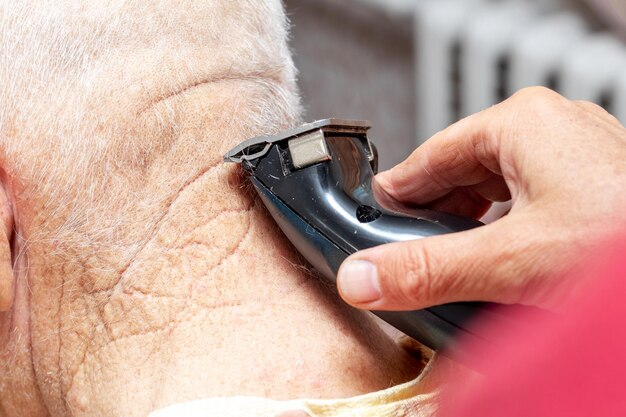 Una mujer corta el pelo en el cuello de un anciano con una recortadora