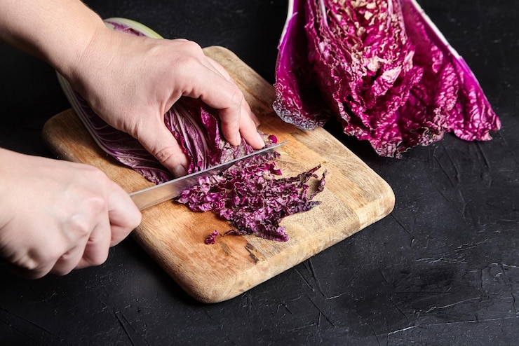 Mujer corta repollo chino rojo Wombok morado sobre tabla de cortar de madera sobre fondo negro Red Napa
