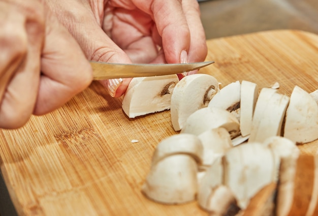 La mujer corta las setas en la tabla de cortar de madera. Cocina según la receta en casa en la cocina.