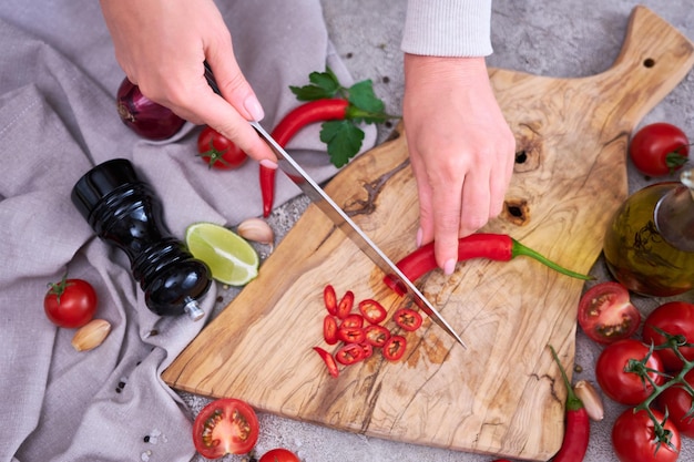 La mujer corta la tabla de cortar de madera de los chiles rojos frescos en la cocina doméstica