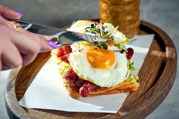 Una mujer corta tostadas con huevos revueltos con salchichas de yema en una tabla de cortar Fondo de hormigón luz de la mañana Huevos para el desayuno