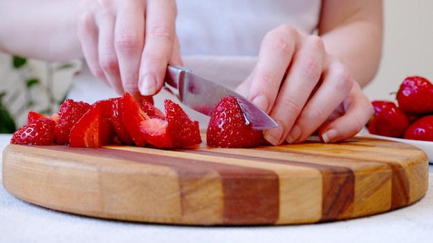 Mujer cortando fresas en tablero de madera y preparando batido o batido