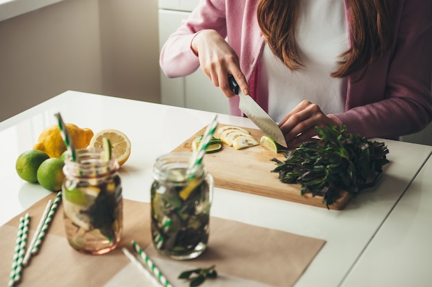 Mujer cortando frutas para hacer un mojito en casa usando limones y menta en jar