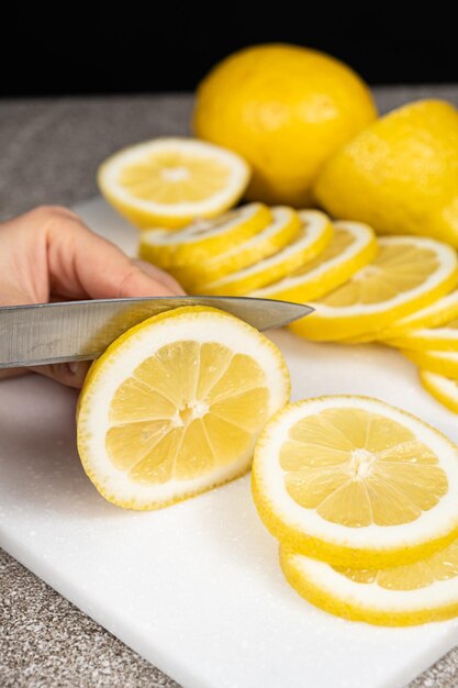 Mujer cortando limón en rebanadas con un cuchillo de utilidad afilado en una tabla de cocina de piedra