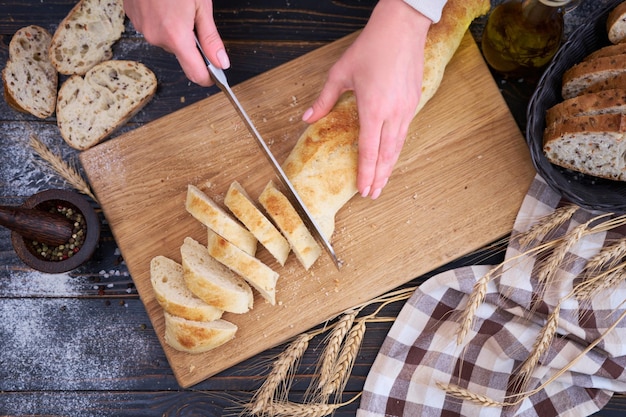 Mujer cortando pan recién horneado en la mesa de la cocina de madera