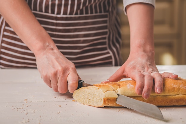 Foto mujer cortando pan sobre tabla de madera. panadería. producción de pan. una mujer con un delantal a rayas