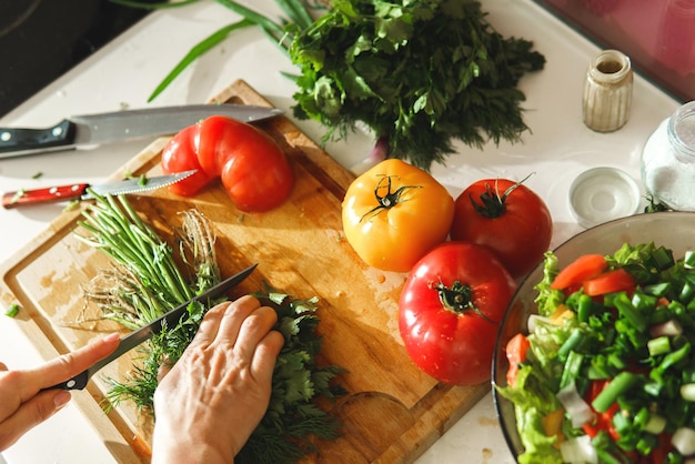 Mujer cortando perejil verde y eneldo para una ensalada vegetariana saludable