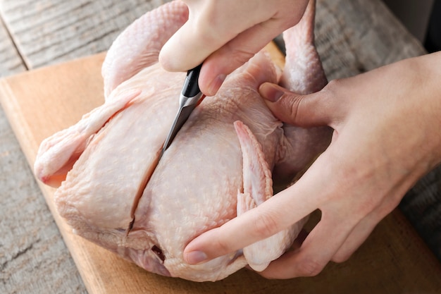 Mujer cortando un pollo con un cuchillo en una tabla de cortar