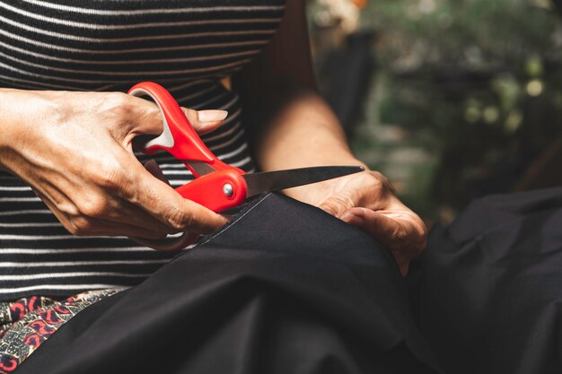 Mujer cortando tela negra con tijeras. Concepto de tareas domésticas y estilo de vida.
