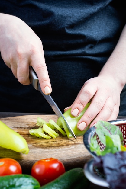 Mujer cortando verduras frescas en una tabla para cortar