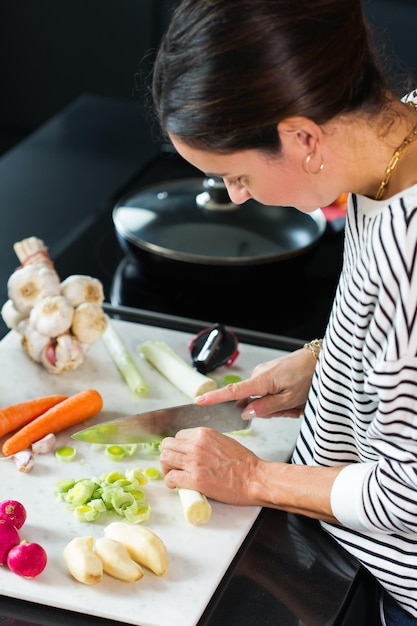 Mujer cortando verduras mientras cocina estofado de cerca de las manos de la mujer cortando hortalizas