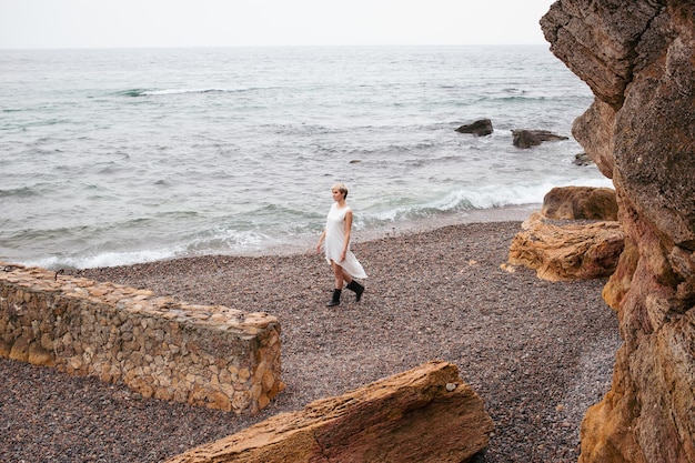 Mujer con corte de pelo corto con vestido cerca del mar y rocas en otoño