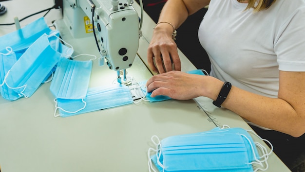 La mujer cose el facial médico en la máquina de coser. Pandemia de coronavirus.