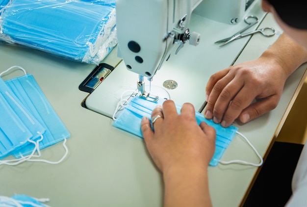 La mujer cose el facial médico en la máquina de coser. Pandemia de coronavirus.