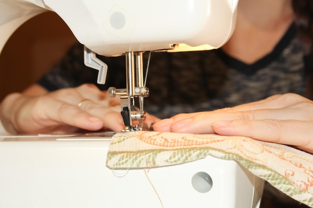 Una mujer cose en una máquina de coser eléctrica blanca. El concepto de costura, corte, costura.