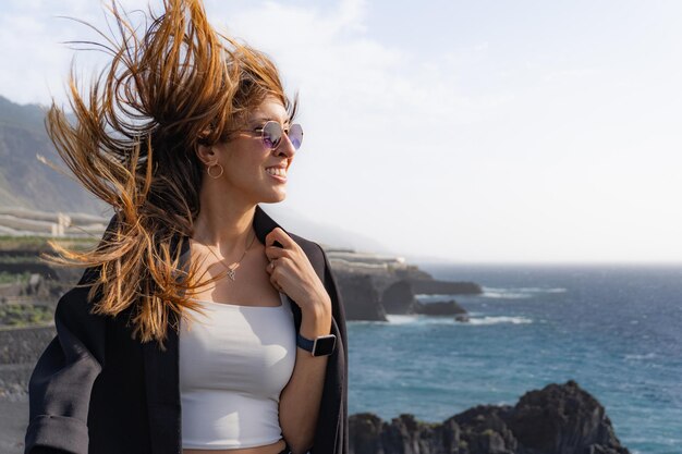 Foto la mujer de costado se pone una chaqueta con el cabello soplado por el viento en los acantilados