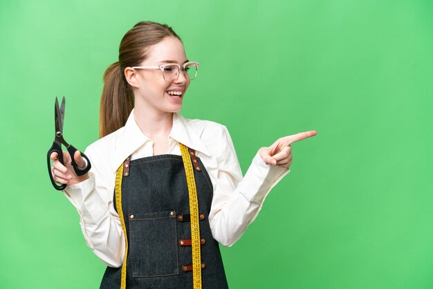 Mujer costurera sobre fondo de clave de croma aislado apuntando con el dedo hacia un lado y presentando un producto