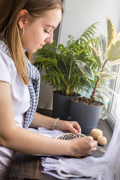 Mujer creadora haciendo atrapasueños étnicos tribales hechos a mano disfrutando del trabajo o pasatiempo en el taller