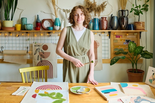 Mujer creativa joven feliz en vestido casual gris con pincel en la mano