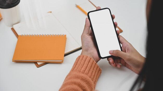 Mujer creativa con smartphone con pantalla vacía en el escritorio.