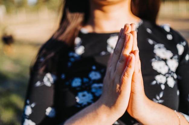 Mujer creyente religiosa orando, juntando las manos para recibir el espíritu de Dios, al atardecer.