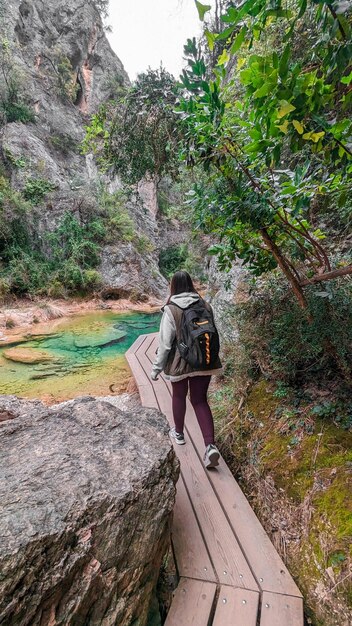 Una mujer cruza un puente de madera que tiene una mochila encima.