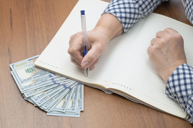 Mujer con un cuaderno, un bolígrafo y una pila de billetes de cien dólares en efectivo en un escritorio