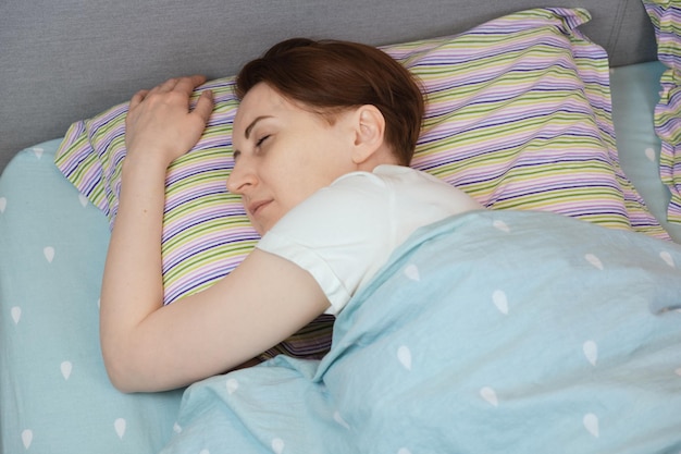 Mujer de cuarenta años durmiendo de lado abrazando una almohada