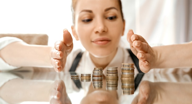 Una mujer cubre ahorra dinero pilas de mesa de monedas. Mira con ahorros. Foto de alta calidad