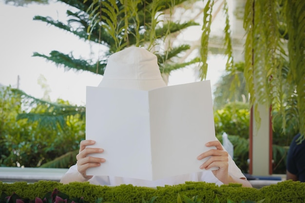 La mujer se cubre la cara con un libro en blanco o una revista en concepto de maqueta.