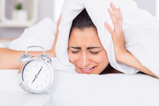 Mujer cubriendo las orejas con la sábana en la cama