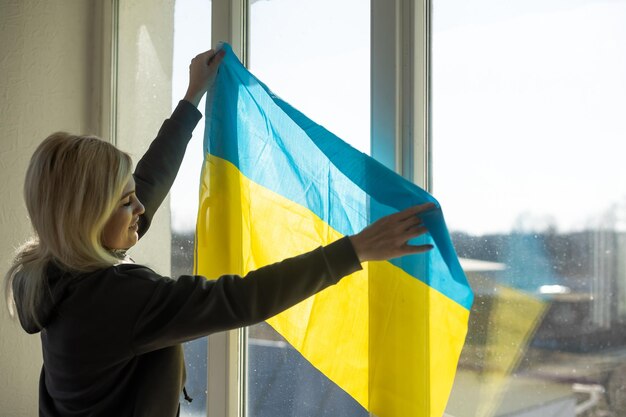 Una mujer cuelga una bandera de ucrania en la ventana.