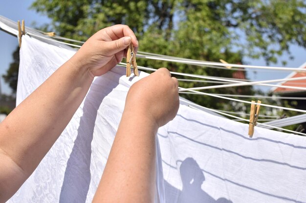 Una mujer cuelga sábanas blancas para que se sequen al aire libre y las sujeta con una pinza para la ropa