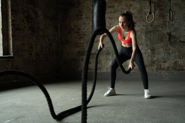 Mujer con cuerdas de batalla ejercicio en el gimnasio deportista trabajando en el gimnasio