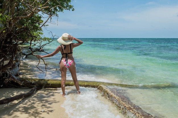 Mujer de cuerpo completo con sombrero y bikini mirando el horizonte de la playa del Mar Caribe en Cartagena