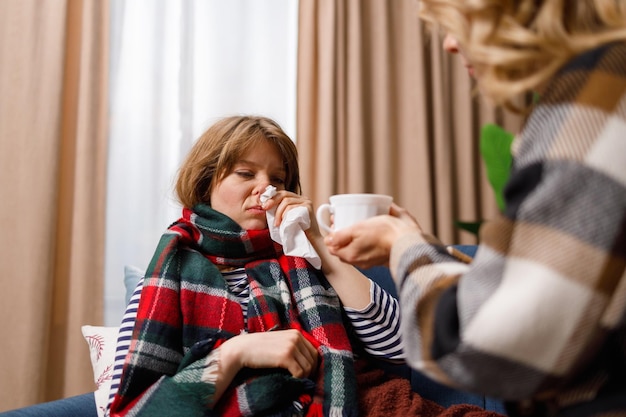 Mujer cuida a su hija que tiene gripe le da té caliente para beber