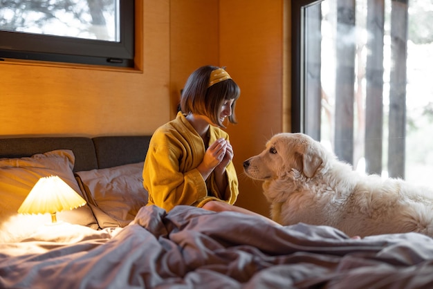 La mujer cuida a su perro mientras está acostada en la cama en un pequeño dormitorio de cabaña de madera en la naturaleza