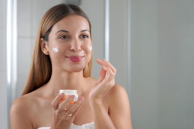 Mujer de cuidado de la piel aplicando crema en la mejilla Tratamientos nutritivos nutritivos hidratantes faciales Disfrutando de un momento relajante