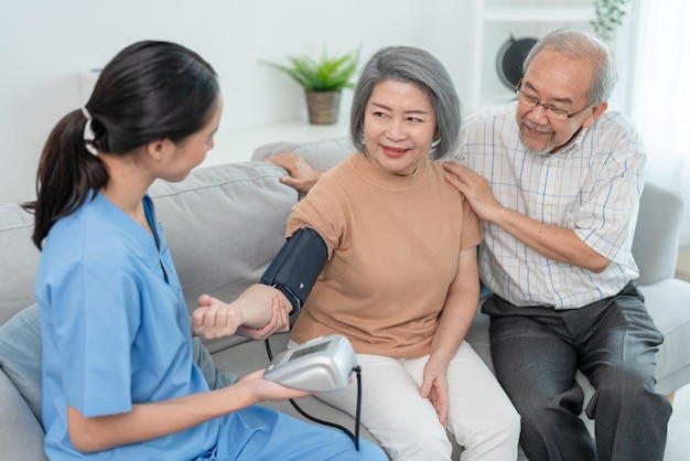 Mujer cuidadora que usa manómetro para medir la presión arterial paciente anciana durante la visita al hogar