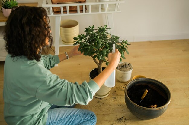 La mujer cultiva plantas en macetas en el hogar, riega y cuida las flores, la jardinería y el cuidado de las plantas domésticas.