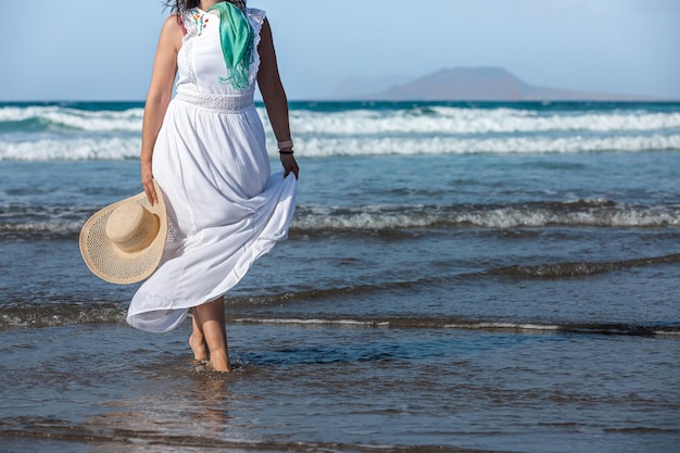 Mujer de cultivo con vestido blanco caminando en el mar agitado