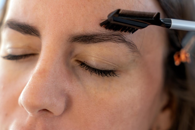 Mujer de cultivos cepillando las cejas durante la rutina diaria de belleza