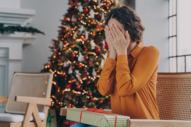 Foto mujer curiosa que cubre los ojos con las manos y adivina qué hay dentro de la caja de regalo de navidad