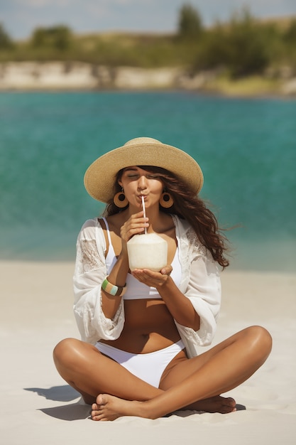 Mujer curtida en bikini con coco en la playa