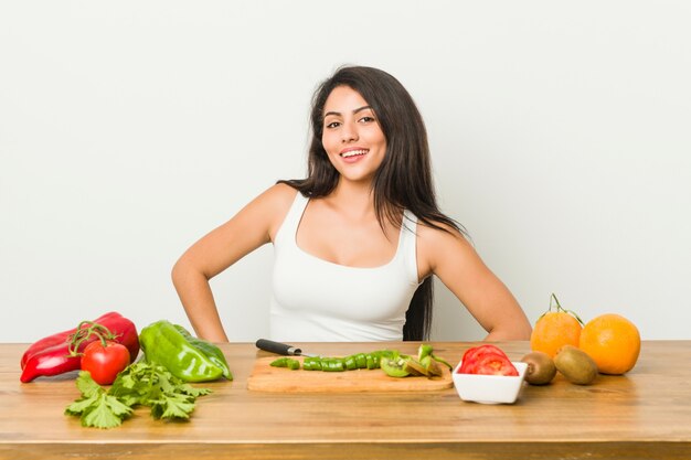 Mujer con curvas joven que prepara una comida sana confiada manteniendo las manos en caderas.