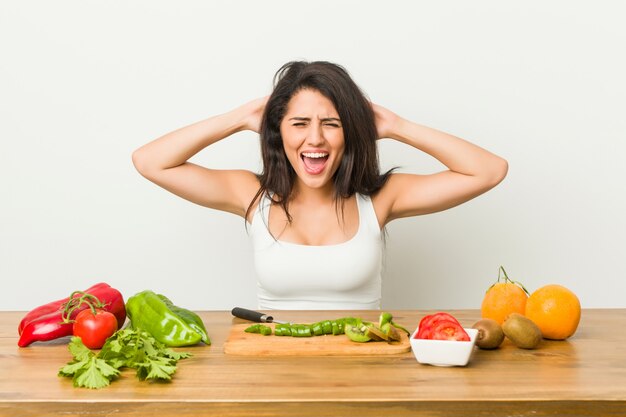 Mujer con curvas joven que prepara una comida sana que cubre los oídos con las manos tratando de no escuchar un sonido demasiado fuerte.